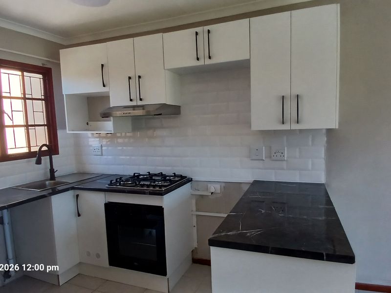 A functional kitchen featuring white cabinetry, dark stone countertops, a gas hob, and a subway tile backsplash, currently awaiting final finishing touches.