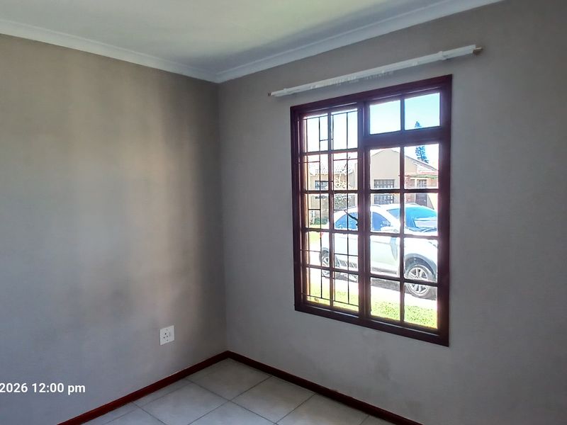 A vacant bedroom featuring tiled flooring, neutral wall paint, and a window fitted with security burglar bars.