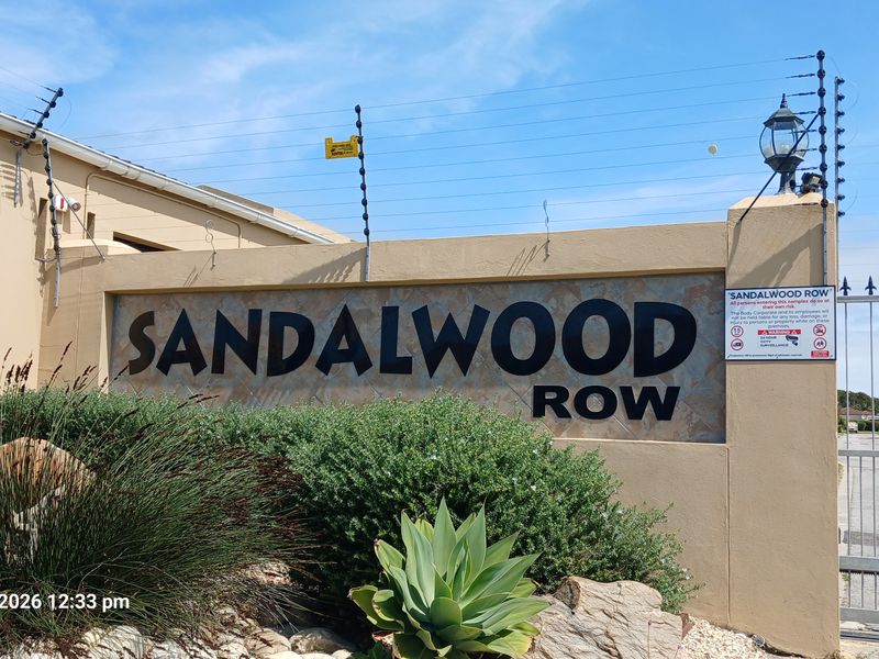 Entrance signage and security gate for Sandalwood Row townhouse complex, featuring masonry boundary wall and electric fencing.