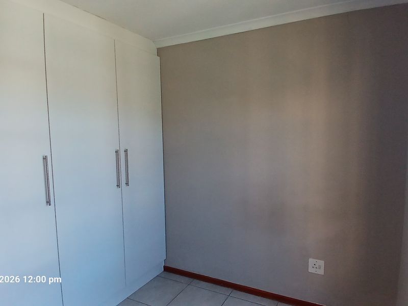 A clean, empty bedroom featuring built-in cupboards, tiled flooring, and security bars on the window.