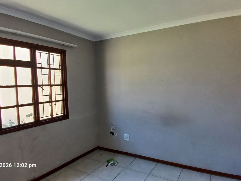 A vacant bedroom featuring tiled flooring, neutral walls, and a wooden window frame with security bars.
