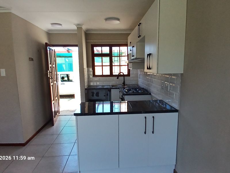 Modern kitchen featuring white cabinetry, granite countertops, subway tile backsplash, and a gas hob, with direct access to the exterior.