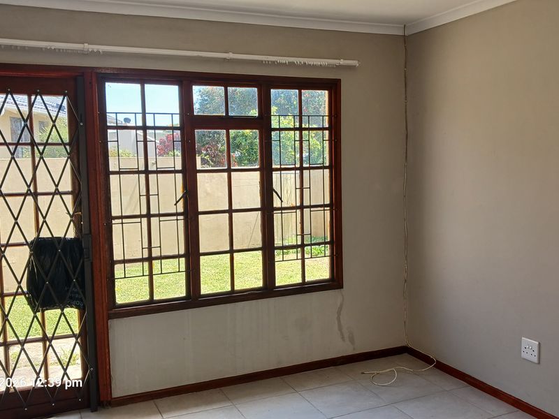 An empty living room featuring tiled floors, wooden window frames, and a security gate, showing signs of wall staining and wear.