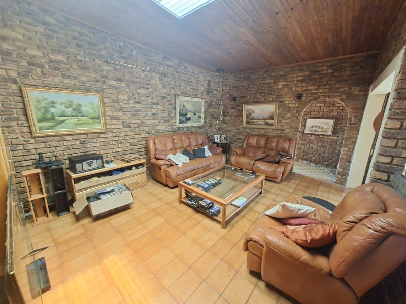 Spacious living room featuring rustic exposed brick walls, a warm timber ceiling with a skylight, and durable tiled flooring with an arched entryway.