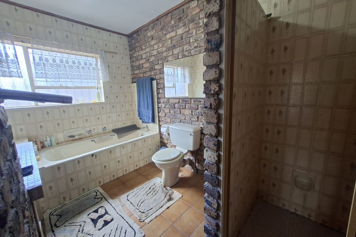 A dated bathroom featuring exposed brick walls, ceramic tiling, a built-in bathtub, and a separate shower enclosure.