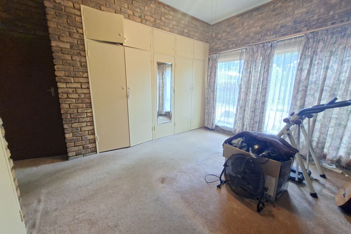 Bedroom featuring exposed brick walls, built-in cupboards with a central mirror, and large windows allowing natural light.