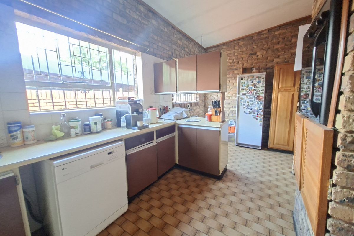 A rustic kitchen featuring exposed brick walls, dated cabinetry, and tiled flooring, offering a functional layout with potential for modern renovation.