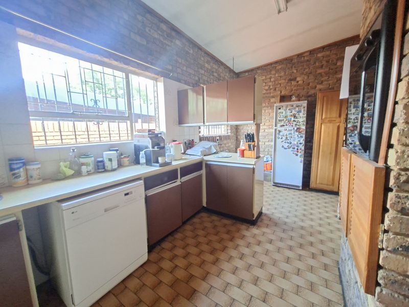 A rustic kitchen featuring exposed brick walls, dated cabinetry, and tiled flooring, offering a functional layout with potential for modern renovation.