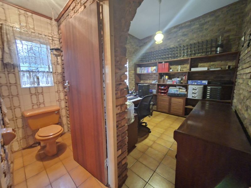A home office space featuring exposed brick walls and built-in shelving, adjacent to a small bathroom with dated fixtures.