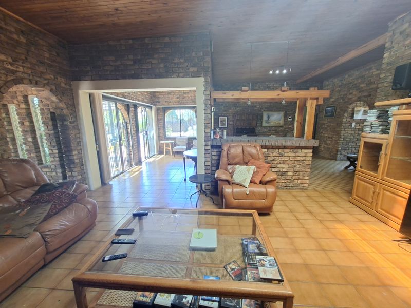 Spacious open-plan living area featuring exposed brick walls, timber ceilings, and a built-in brick bar, offering a rustic aesthetic with direct access to the patio.