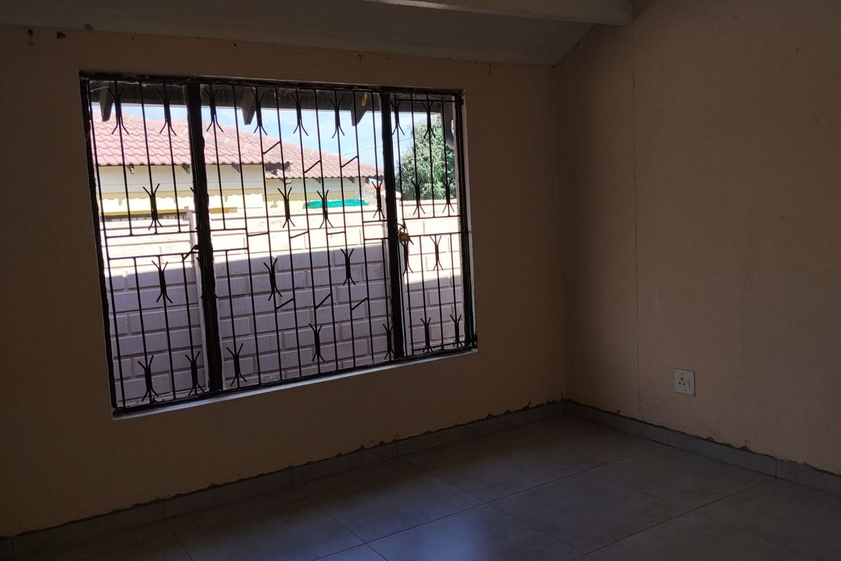 An empty bedroom featuring tiled flooring and security burglar bars on the window, requiring minor cosmetic attention to the wall finishes.