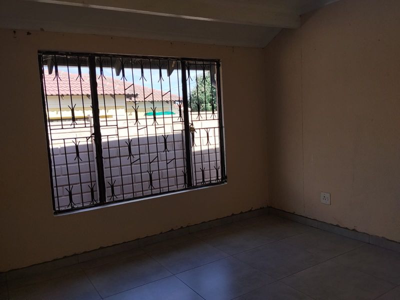 An empty bedroom featuring tiled flooring and security burglar bars on the window, requiring minor cosmetic attention to the wall finishes.