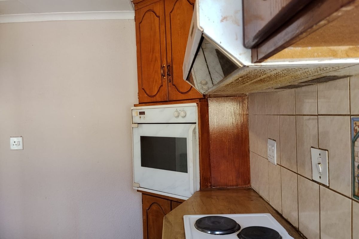 A dated kitchen featuring wooden cabinetry, a built-in oven, and an electric hob with a tiled backsplash.