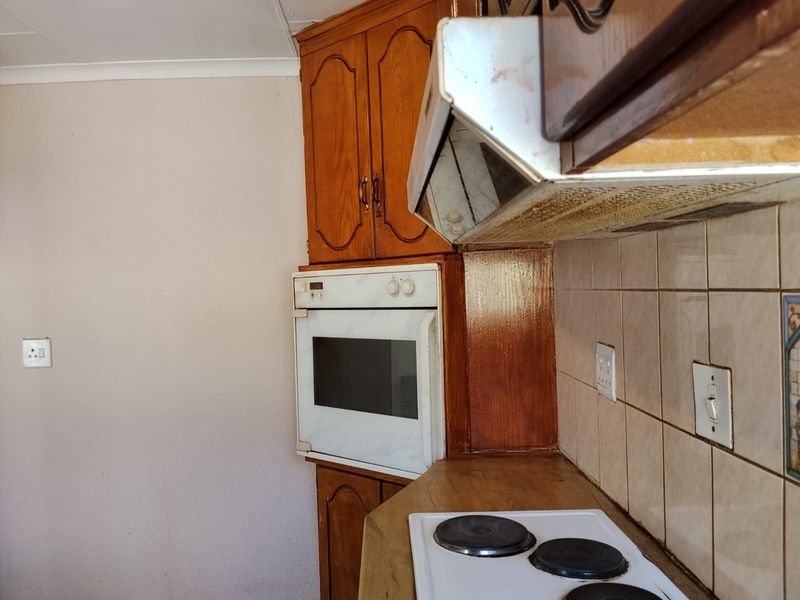 A dated kitchen featuring wooden cabinetry, a built-in oven, and an electric hob with a tiled backsplash.