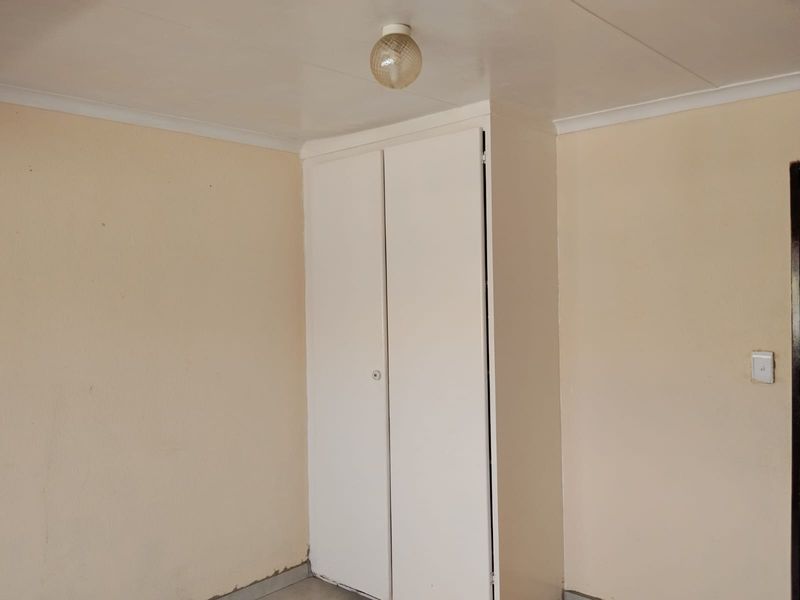 An empty bedroom featuring a built-in wardrobe, neutral wall paint, and a simple ceiling light fixture, ready for personal touches.