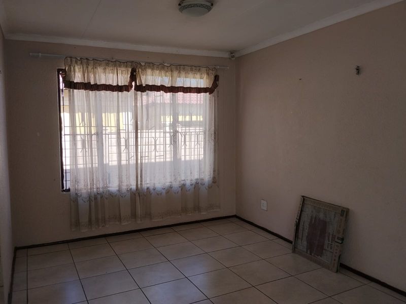 An empty bedroom featuring tiled flooring, security bars on the window, and neutral wall finishes, offering a blank canvas for personalization.