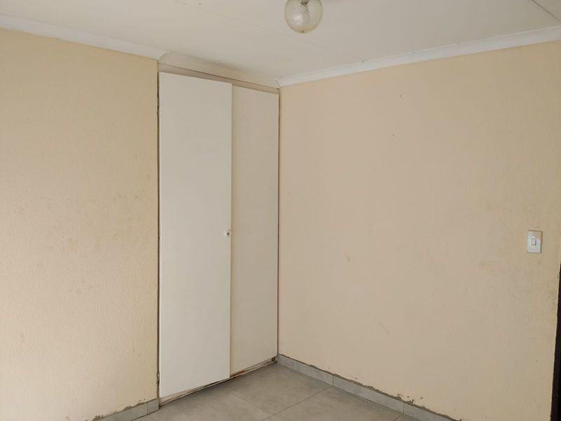 An empty bedroom featuring tiled flooring, a built-in cupboard, and neutral wall finishes, offering a blank canvas for potential interior updates.