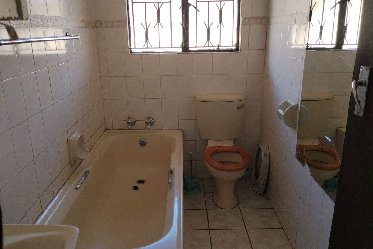 A dated bathroom featuring a bathtub, toilet, and tiled finishes. The space is ready for modernization and renovation to improve its overall aesthetic and functionality.