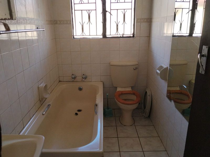 A dated bathroom featuring a bathtub, toilet, and tiled finishes. The space is ready for modernization and renovation to improve its overall aesthetic and functionality.