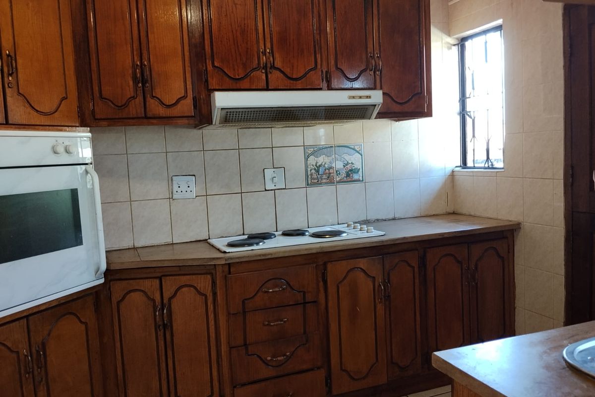 A traditional kitchen featuring dark wood cabinetry, built-in oven, electric hob, and tiled backsplash, offering a functional layout with potential for modern updates.
