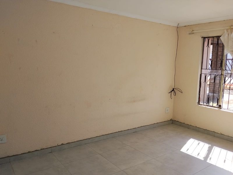 An empty bedroom featuring tiled flooring, security bars on the window, and neutral wall finishes, ready for a fresh coat of paint and styling.