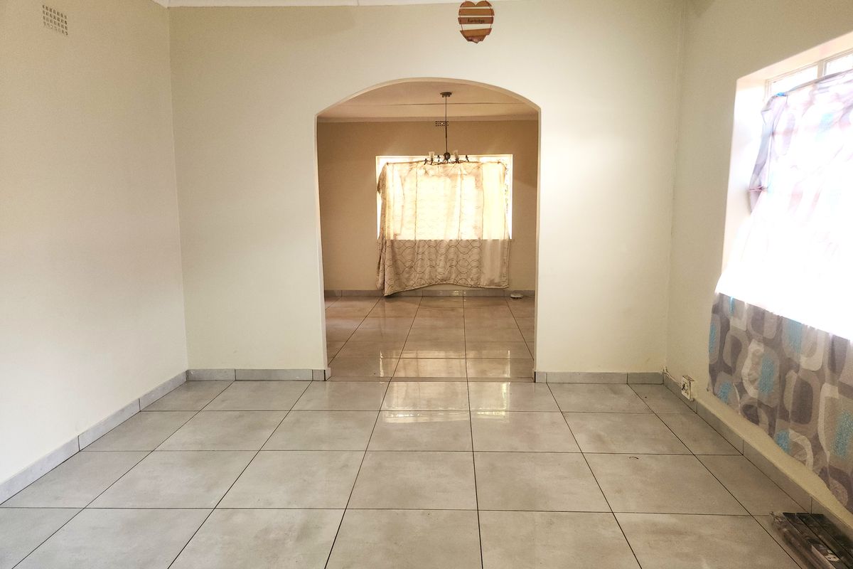 An empty living area featuring neutral tiled flooring, a central archway leading to an adjacent room, and a ceiling fan.