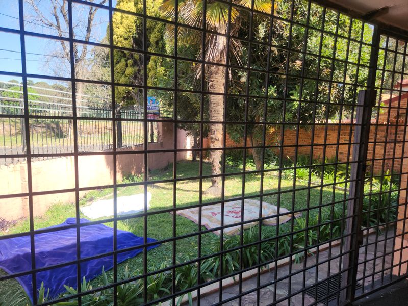 A private garden area enclosed by brick boundary walls and metal security fencing, featuring established trees and a paved walkway.
