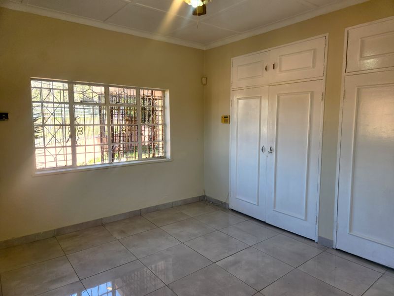 A clean, empty bedroom featuring tiled flooring, built-in cupboards, and security bars on the window.