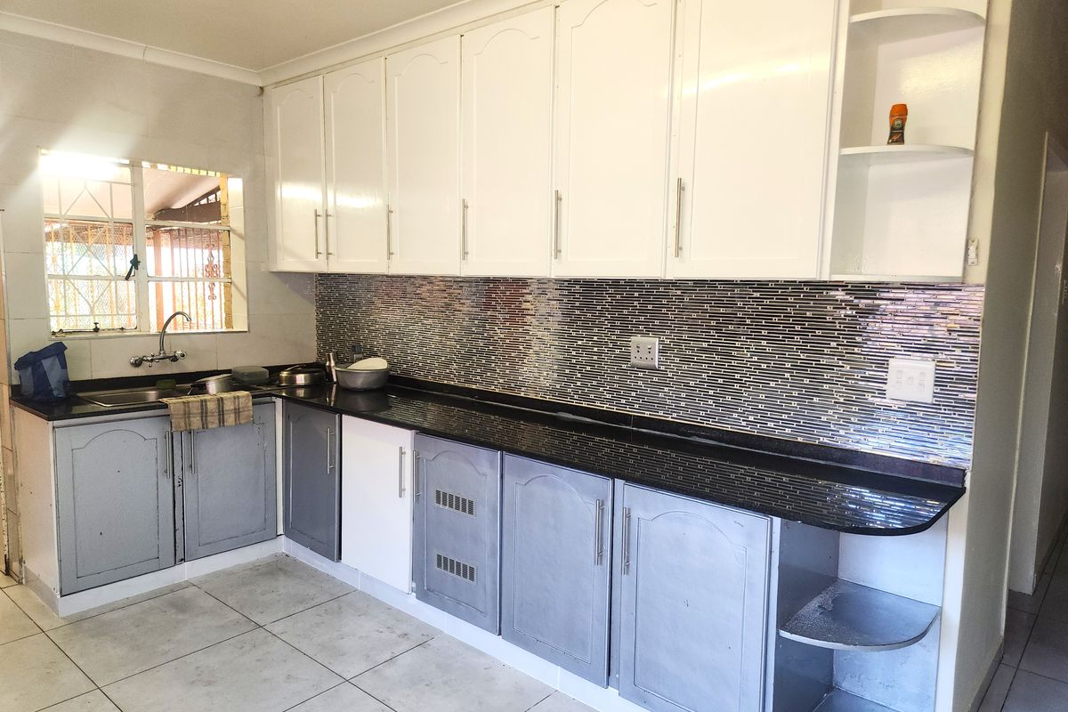 A functional kitchen featuring granite countertops, a mosaic tile backsplash, and ample built-in cabinetry with a mix of white and grey finishes.