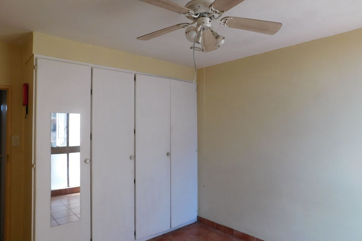 A vacant bedroom featuring built-in cupboards with a mirrored panel, tiled flooring, and a ceiling fan, offering a blank canvas for personalization.