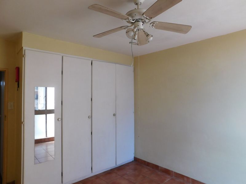 A vacant bedroom featuring built-in cupboards with a mirrored panel, tiled flooring, and a ceiling fan, offering a blank canvas for personalization.