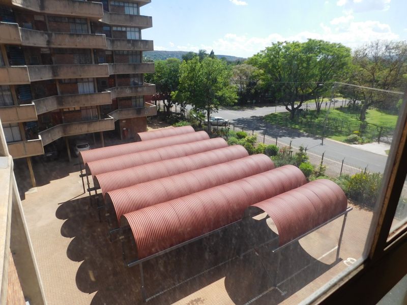Elevated view overlooking the apartment complex parking area featuring multiple covered parking bays with corrugated metal roofing.