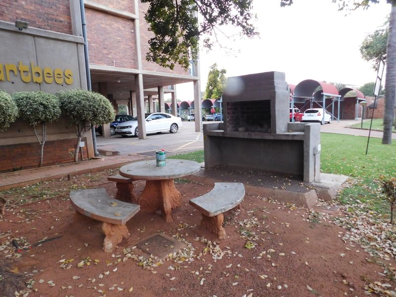 Outdoor communal area featuring a built-in brick braai, concrete seating, and access to covered parking facilities.