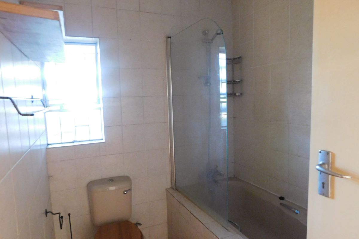 A functional bathroom featuring a bathtub with a glass shower screen, tiled walls, and standard sanitaryware, offering potential for modern updates.