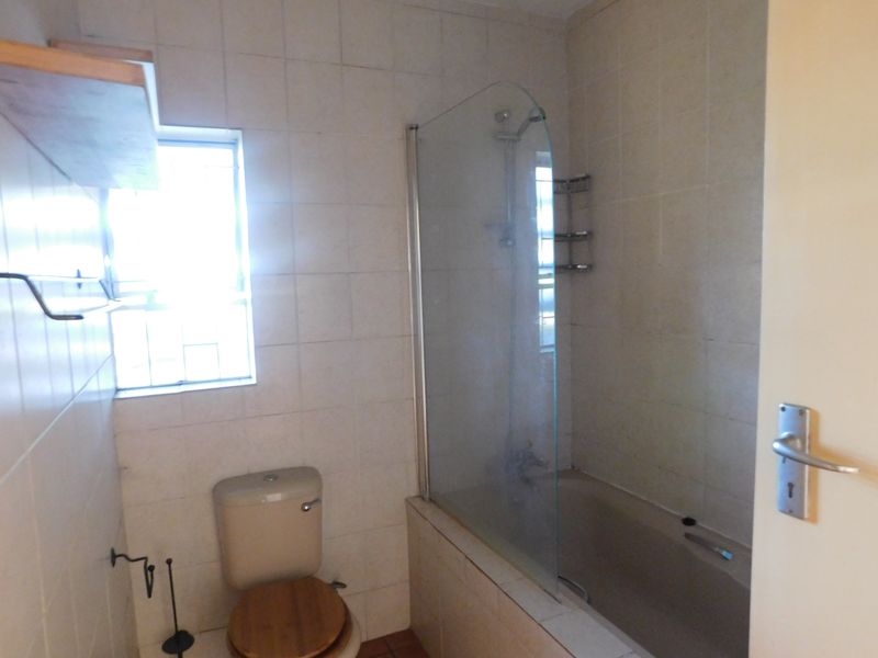 A functional bathroom featuring a bathtub with a glass shower screen, tiled walls, and standard sanitaryware, offering potential for modern updates.