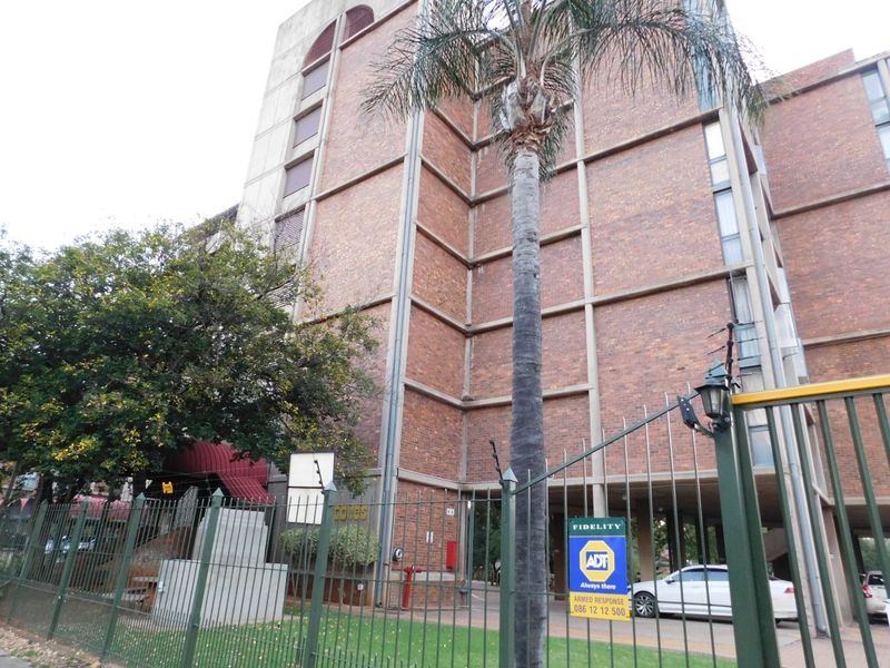 Exterior view of a multi-story brick apartment building featuring concrete structural columns and secure perimeter fencing.