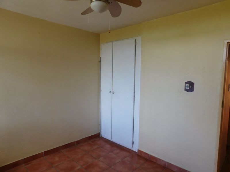 An empty bedroom featuring tiled flooring, a built-in cupboard, and a ceiling fan, offering a blank canvas for personalization.