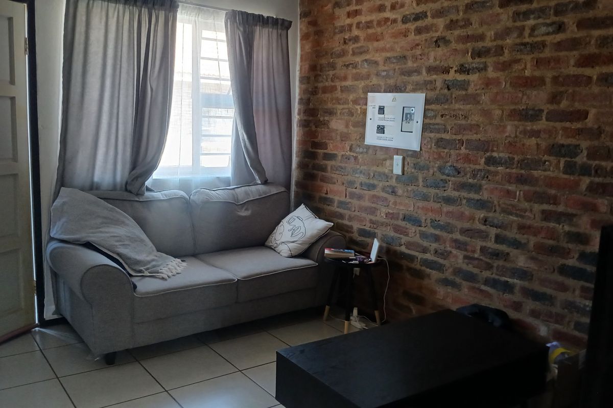 A living room featuring an exposed brick feature wall, tiled flooring, and a window with security bars.