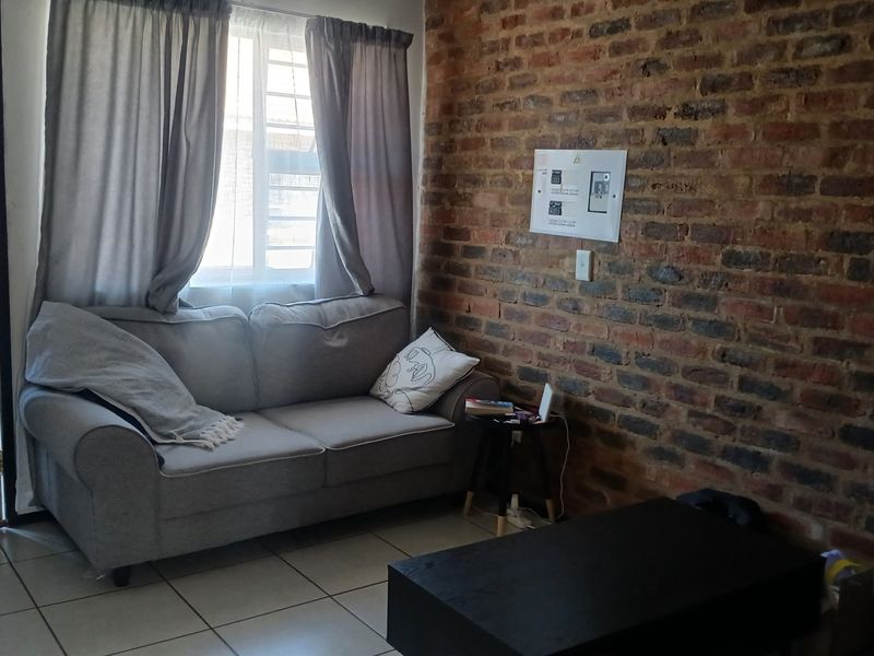A living room featuring an exposed brick feature wall, tiled flooring, and a window with security bars.