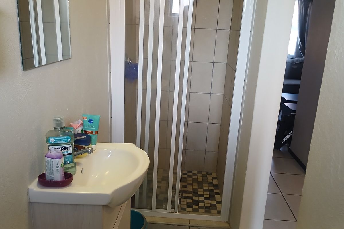 A functional bathroom featuring a pedestal washbasin, a shower enclosure with tiled walls and flooring, and neutral wall finishes.