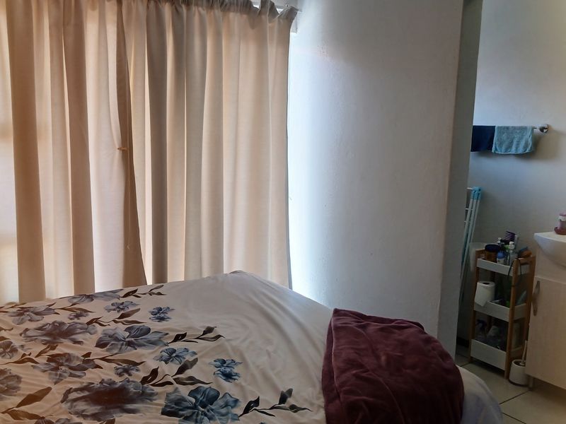 Bedroom featuring an en-suite vanity area with a wall-mounted basin and cabinet, complemented by neutral curtains.