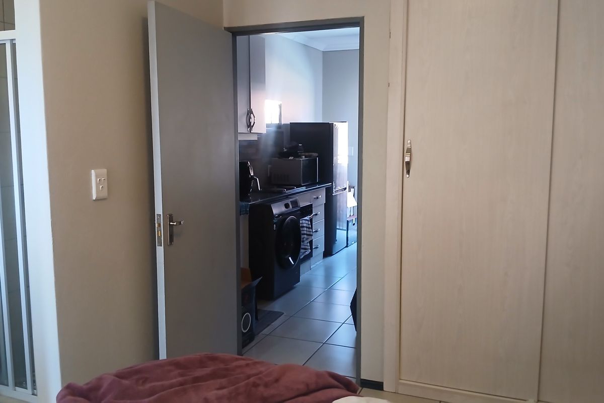 Bedroom featuring built-in wardrobes and tiled flooring, with an adjacent view into the kitchen area.
