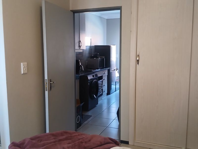 Bedroom featuring built-in wardrobes and tiled flooring, with an adjacent view into the kitchen area.