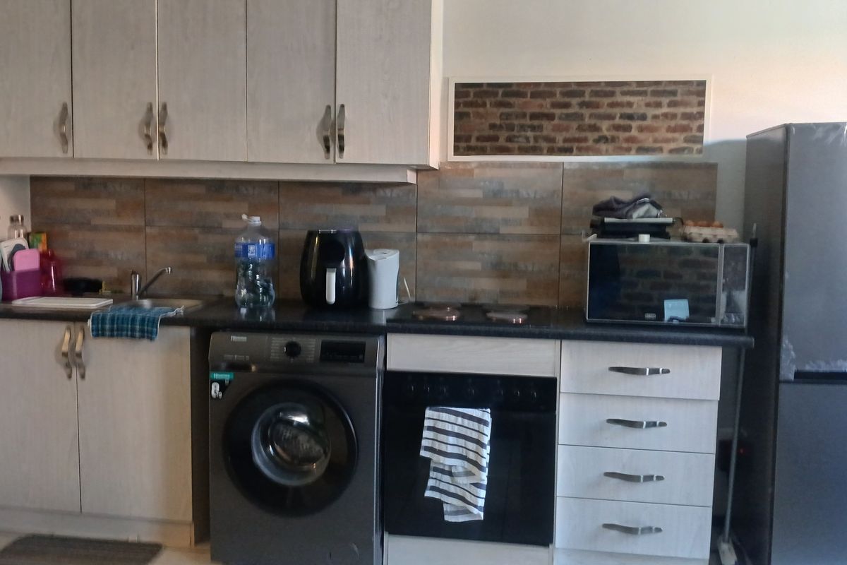 A functional kitchen featuring light-toned cabinetry, dark countertops, a tiled backsplash, and integrated space for a washing machine and oven.
