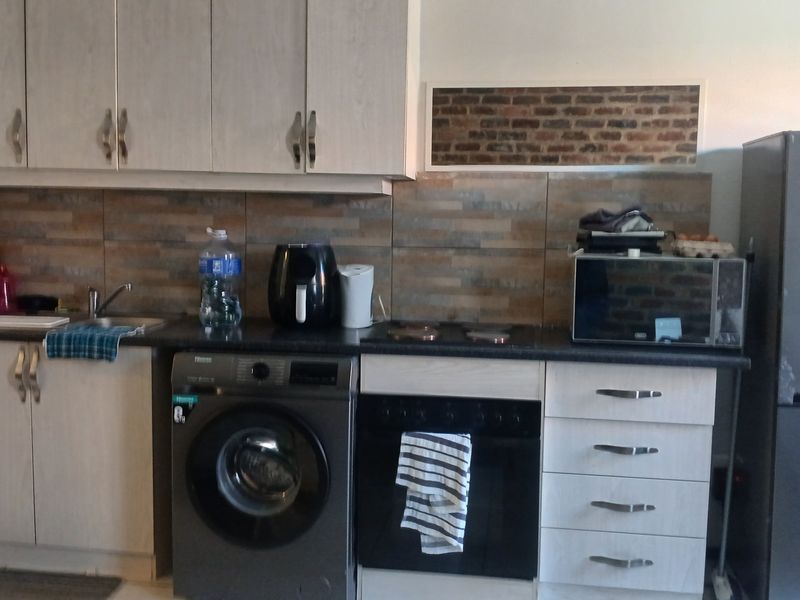 A functional kitchen featuring light-toned cabinetry, dark countertops, a tiled backsplash, and integrated space for a washing machine and oven.