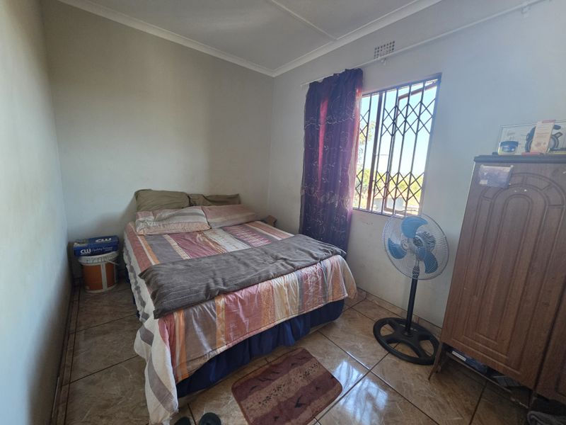 A compact bedroom featuring tiled flooring, a window with security bars, and a security gate, offering a functional space with potential for cosmetic updates.