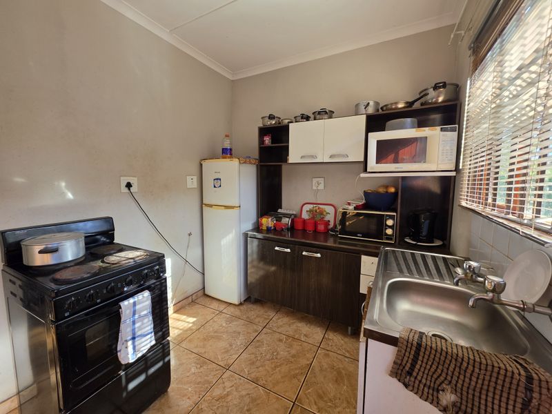 Compact kitchen featuring tiled flooring, built-in cabinetry, a stainless steel sink, and a freestanding stove, offering a functional layout with potential for modernization.