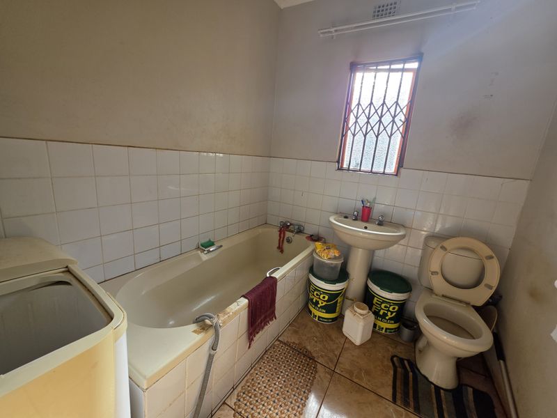 A dated bathroom featuring a bathtub, pedestal basin, and toilet, requiring cosmetic updates and refurbishment to improve its overall condition and appeal.