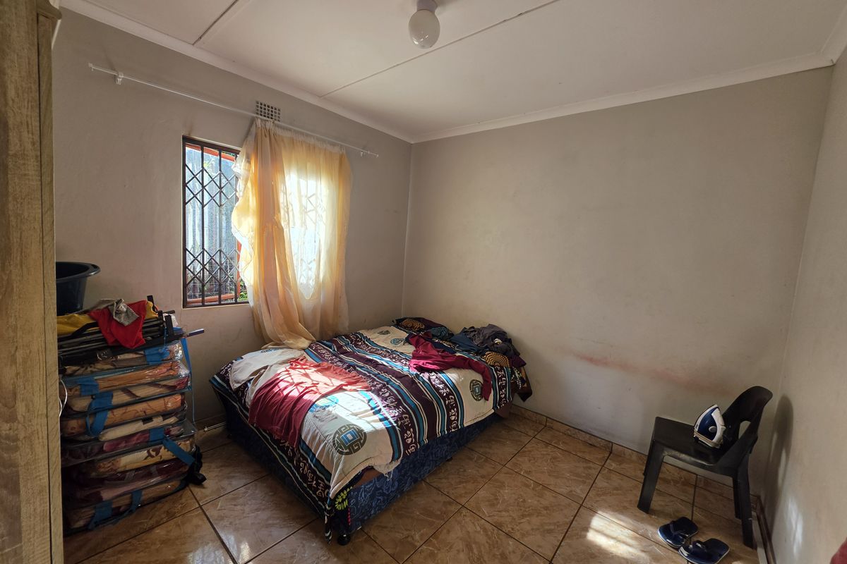 A bedroom featuring tiled flooring and a security gate on the window. The space requires cosmetic updates to the wall finishes.
