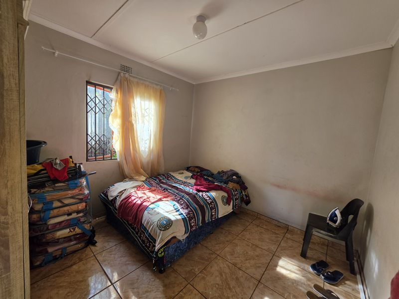A bedroom featuring tiled flooring and a security gate on the window. The space requires cosmetic updates to the wall finishes.